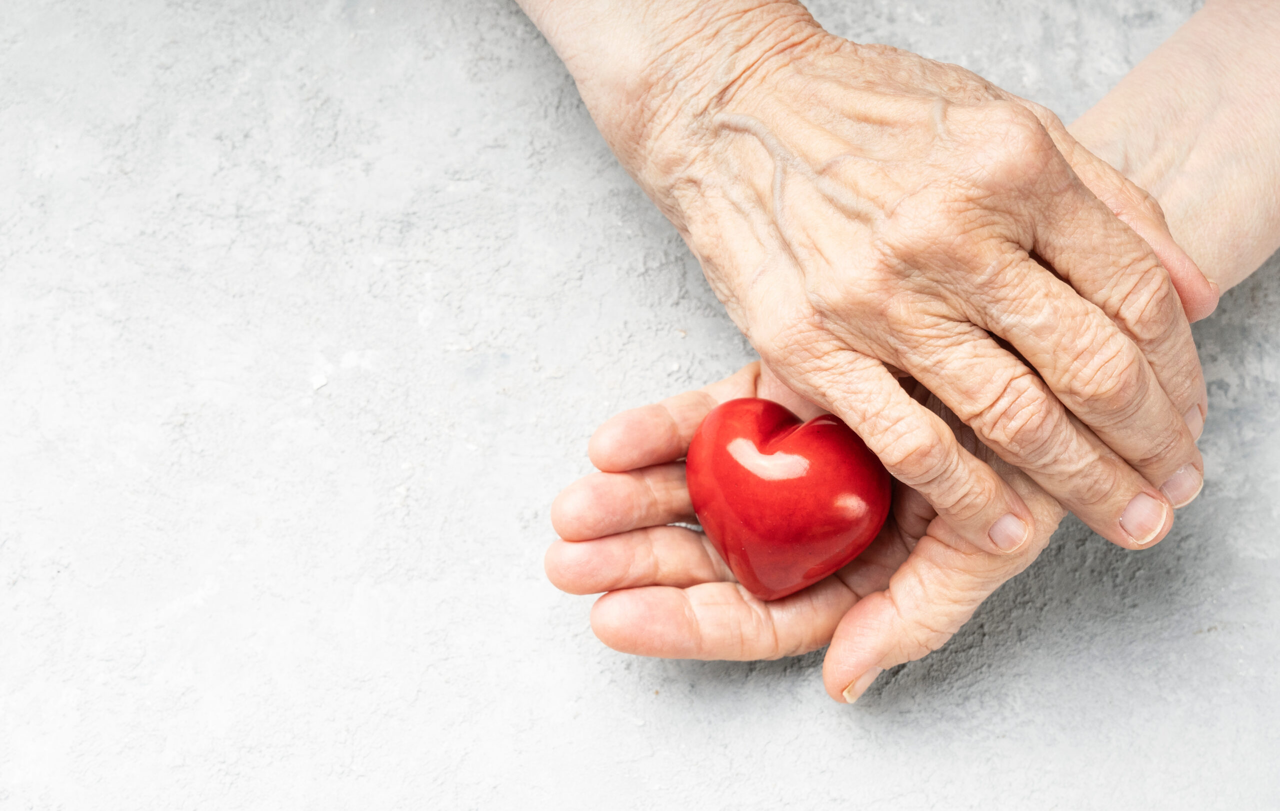 Giving. Wrinkled hands holding red heart symbol. Background with copy space.