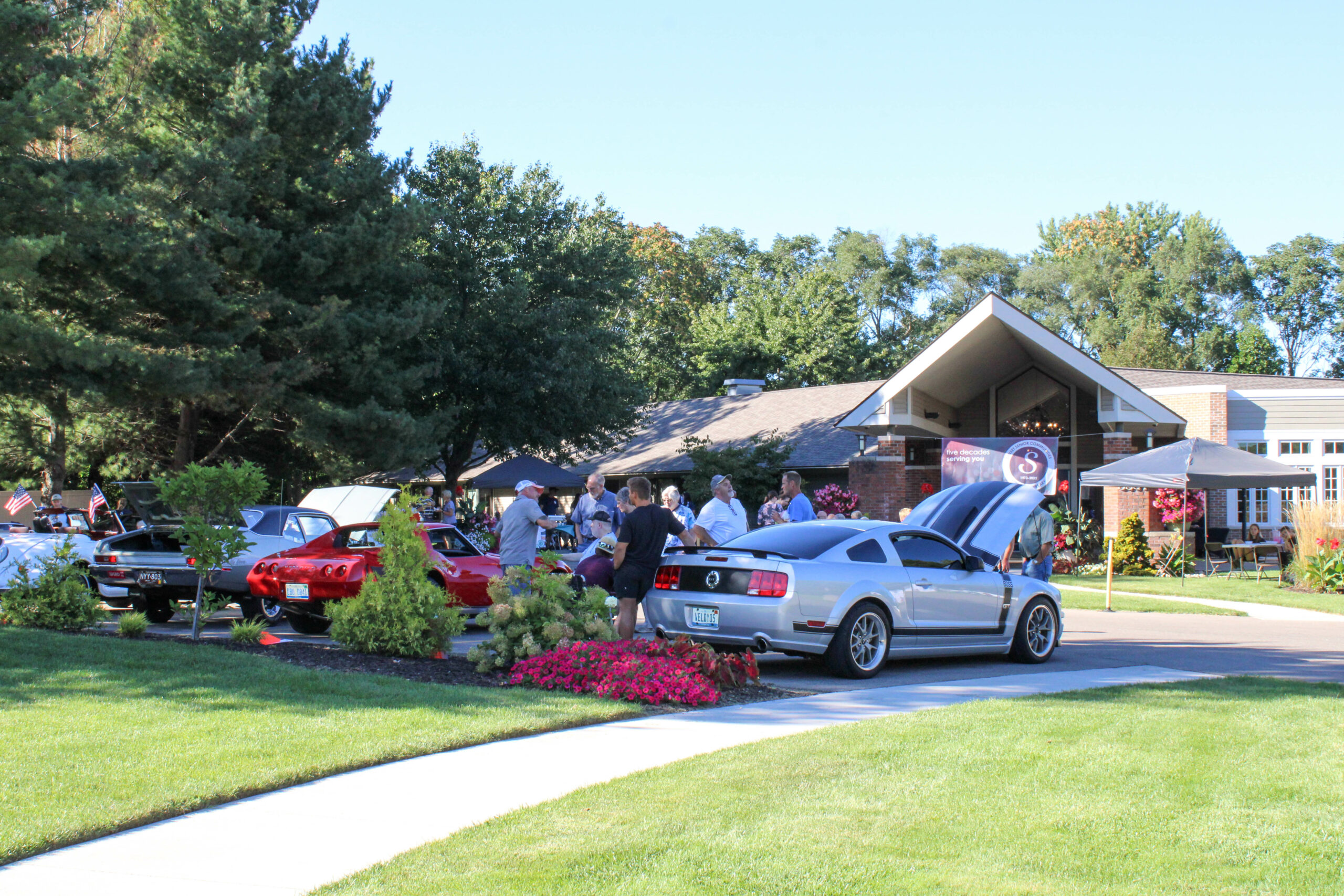 People viewing vehicles in the Rose Garden parking lot during a car show.
