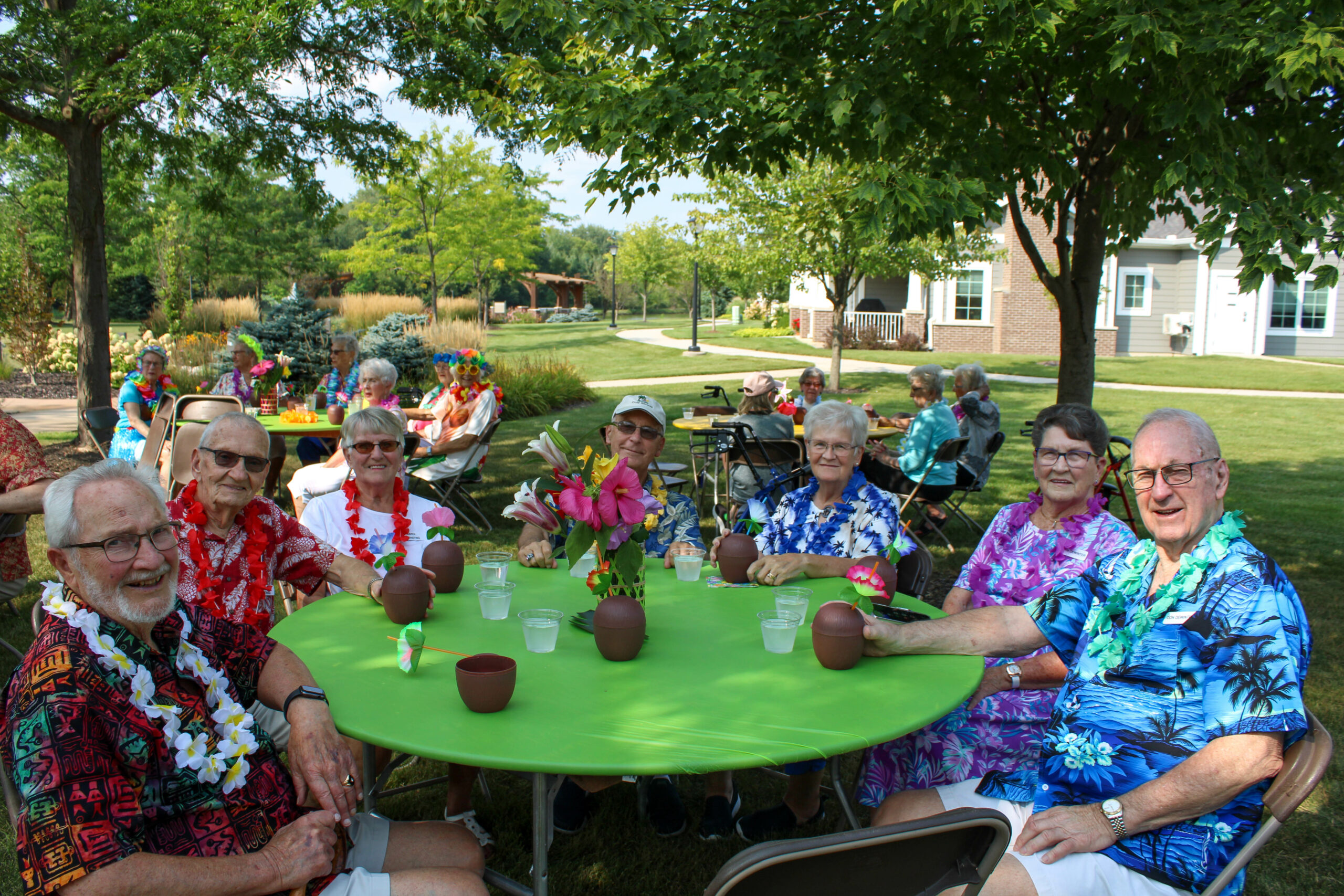 Seniors sitting around a table outside, enjoying a luau event.
