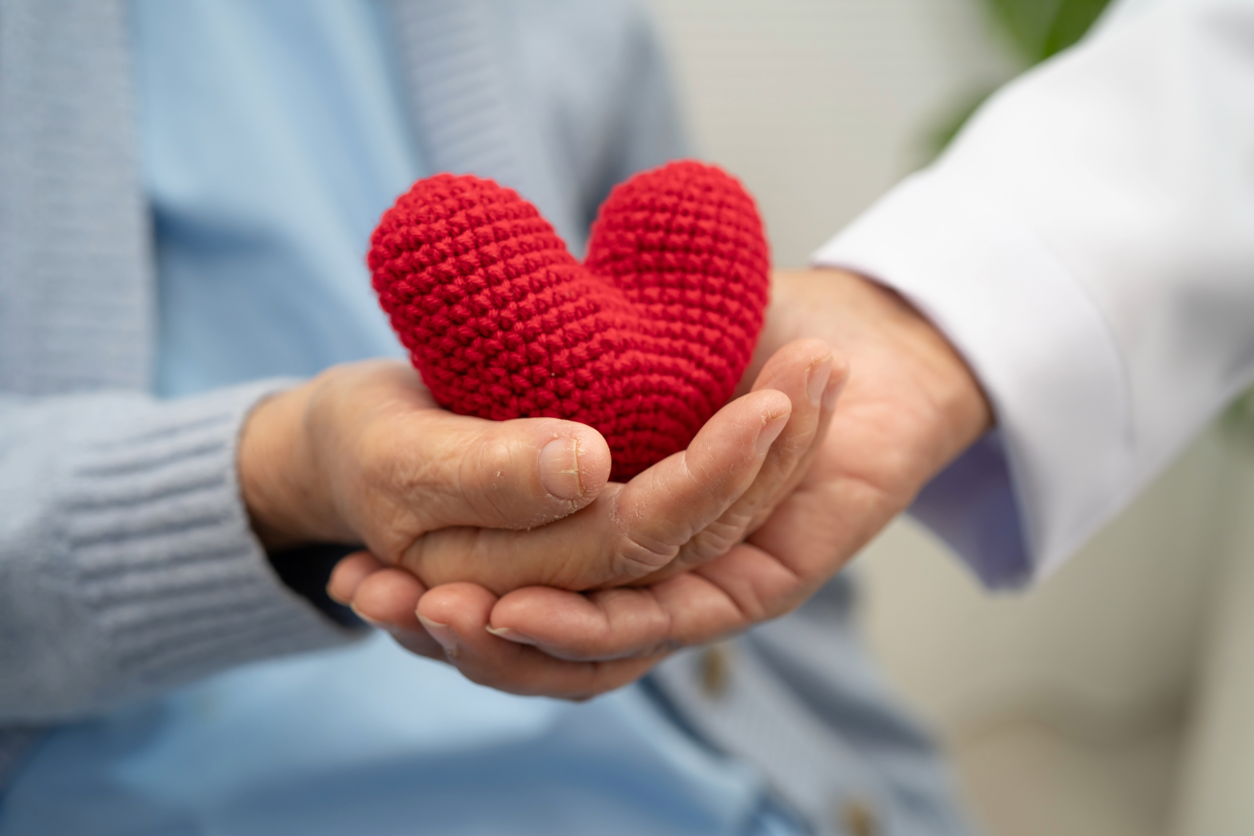 two hands holding a knit red heart.